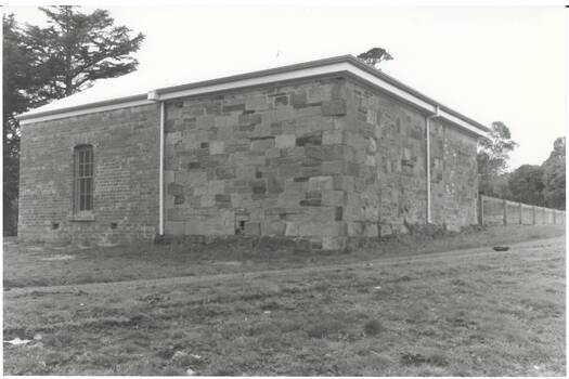 Building, left side brick with narrow window, right side sandstone, low iron roof.