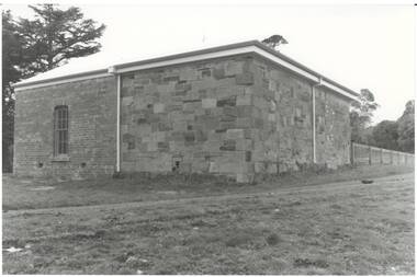 Building, left side brick with narrow window, right side sandstone, low iron roof.