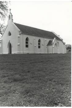 Medium sized Victorian rendered church, gothic window and door frames, slate roof, bell frame on peak of roof.