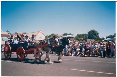 Festical Procession, horse and wagon with red wheels, people in period dress inside, crowd on other side of road.