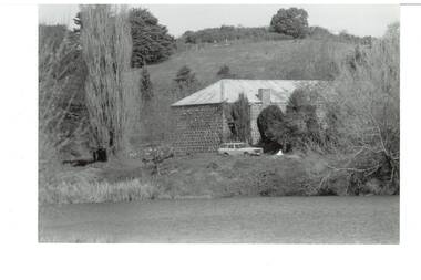 Bluestone, iron-roofed  building, nestled between trees, hill rising behind, reservoir in foreground