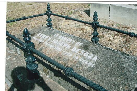 Colour photo, grave with piched "roof" lid, cast iron fence on stone base, inlaid inscription,