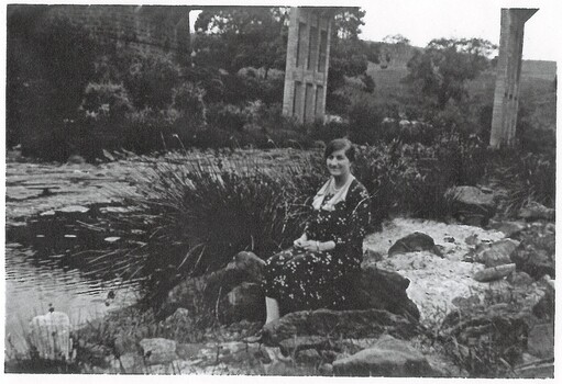 Mt Mercer Junction Bridge. A woman, Elsie Gibson, is sitting on the river bank with the bridge in the background.