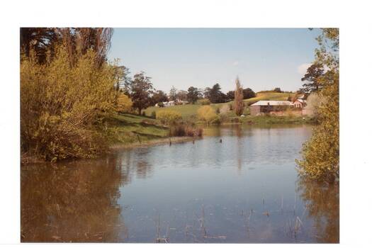 Looking across body of water, trees either side, hills beyond, long stone building upper right, more building upper centre.