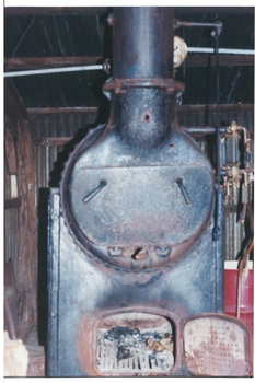 Iron boiler, fire door is open coals inside.