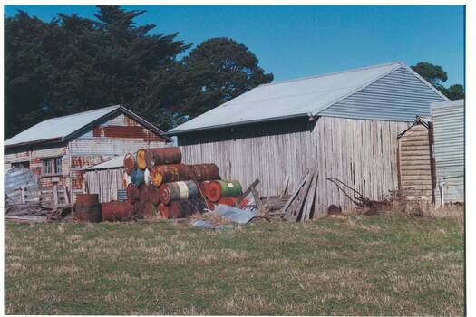 Rusty tin shed on left, wooden shed right, tin roofs, pile of rusted 44 gallon drums