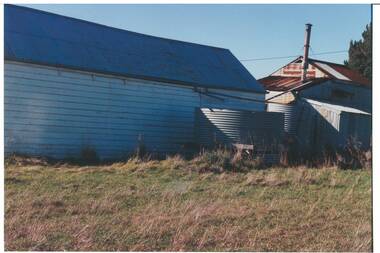 Wooden shed, tin roof, rusted tin shed behind, two iron water tanks.