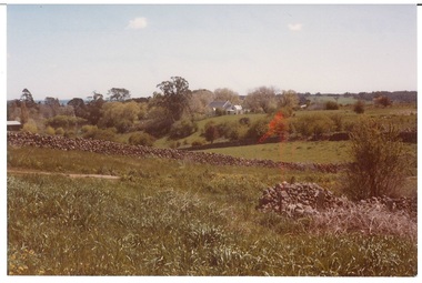 View across hills, lush grass, drystone wall running across, church in background.