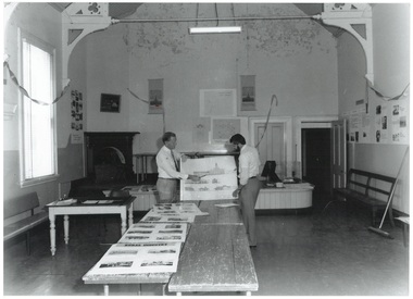 Interior of Courthouse, two men discussing plans, trestles with plans, walls stained.