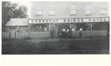Two story wooden building, large sign, picket fence, a man, four women, three children, one dog near entrance,  Post Office lean-to on left.