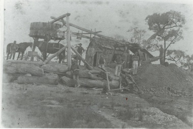 Mine, miners and two horses around rough wooden construction, hut and "Whim" on a mound