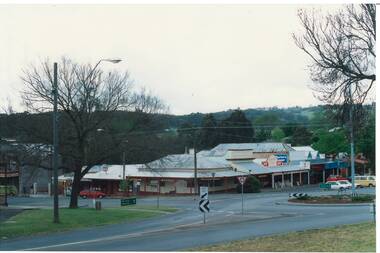 Intersection, roundabout, shops, parked cars, hills in background. 