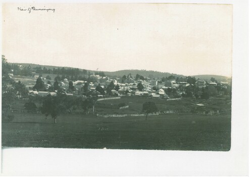 View of Buninyong looking down from south east around 1900, looking across fields and wetland to town surrounded by hills.