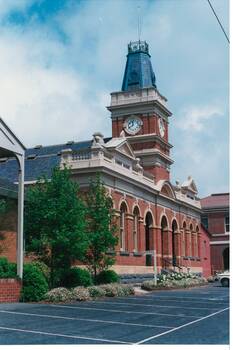 Angle view of italianate polychrome brick building, arched windows, recessed triple arched balcony, square clock tower. 