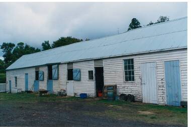 Long weatherboard  building, whitewashed, blue doors, tin roof. Stable doors top half open.