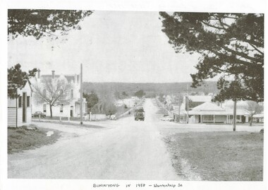 View across intersection, unmade roads, shed and hotel on left, Truck heading down road, shops on right.
