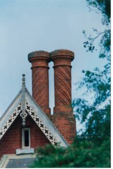 Pair of circular brick chimneys, candy-stripe pattern, above gable with wood carved decoration.