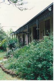 Looking through garden to veranda with wooden posts and iron lace-work.