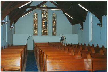 Interior of church, cream walls, wooden pews, vaulted ceiling, Three very tall Gothjic stained-glass windows.