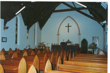 Interior of church, white walls, pews, tall gothic  windows, communion table and pulpit. False archway on wall around large cross.
