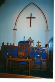 Interior of church, carved wooden pulpit, chairs and Communion Table, arch and cross on wall behind.