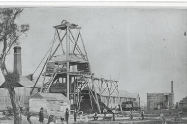 Mine structures including wooden poppet, sheds, two brick chimneys, railway engine and freight wagon, men and a dog middle distnce.