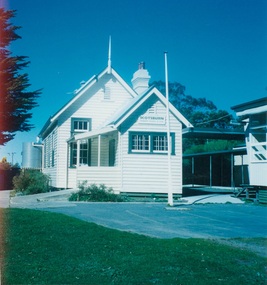 White woden school building, high peaked roof, small extended section at front with verandah