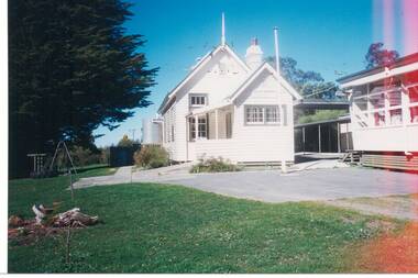White weatherboard school building, modern classroom on right, flagpole, grounds and some play equipment