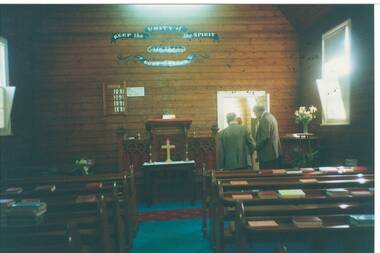 Interior church, unpainted wood-lined walls, communion table, pews with hymnals