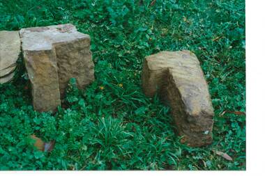 Three rough hewn, irregular shaped sandstone blocks, lying on grass.