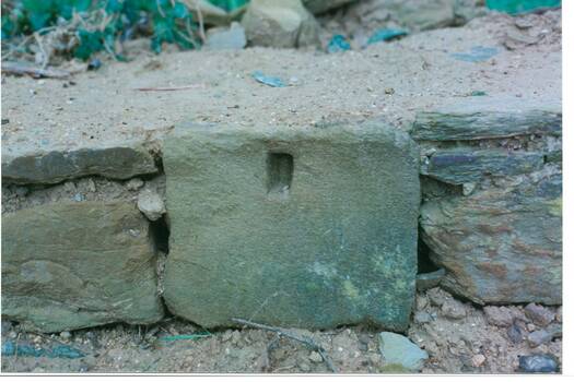 Section of wall showing three sandstone blocks at ground level, one showing hole for sppory of a wooden strut.