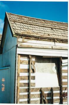 Cottage under demolition, close up, walls stripped, struts showing, window frame removed, fibro cladding on side.