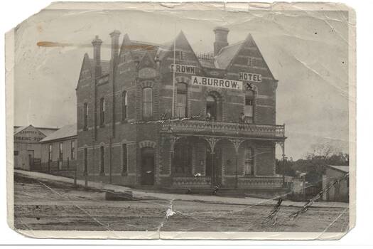 Tall, gabled two story hotel, polychrome brick on corner, full width iron lace veranda across front