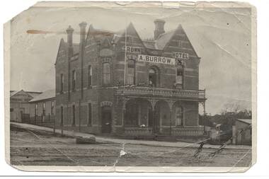 Tall, gabled two story hotel, polychrome brick on corner, full width iron lace veranda across front
