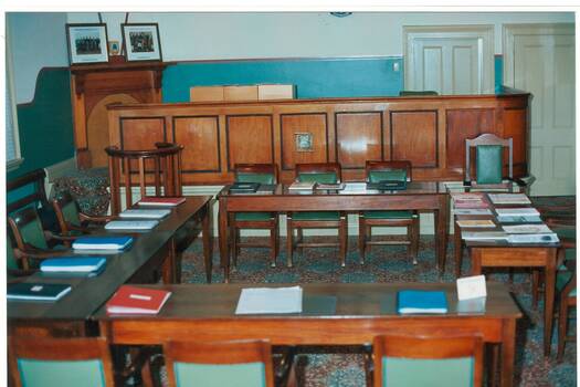 large room, cream walls with green dado, tables and chairs with books, arranged in open square.