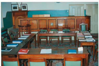 large room, cream walls with green dado, tables and chairs with books, arranged in open square.
