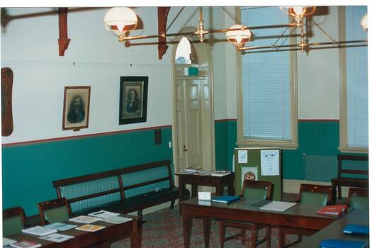 Interior Buninyong Courthouse, view to NW corner showing entrance door, tall windows with venetian blinds, hanging brass lamps.