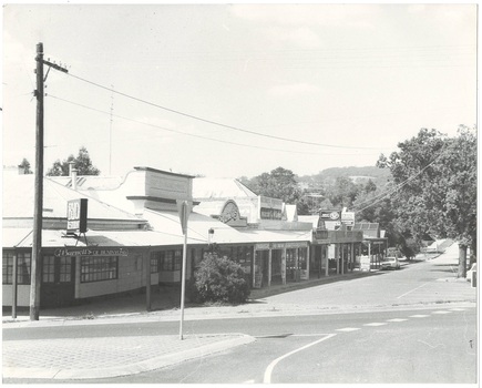 Row of shops from intersection, down service road, all with veranda, all single story but different heights, tree on right, mount at rear.