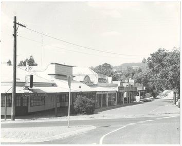 Row of shops from intersection, down service road, all with veranda, all single story but different heights, tree on right, mount at rear.