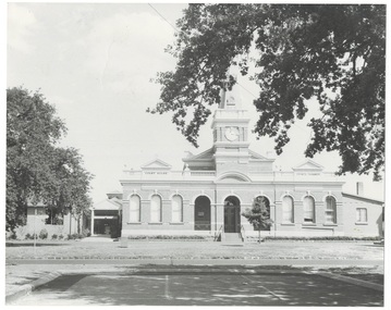 Town Hall, front, italianate polychrome brick with clock tower, trees and parking in foreground.