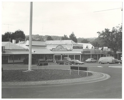 row of shops, SIngle story looking across roundfabout, cars, truck and van parked in front.