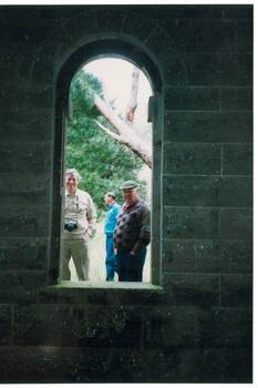 Inside tower, bluestone walls, looking out through tall, arched window, two men looking in.