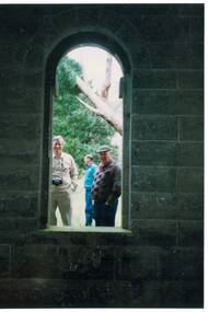 Inside tower, bluestone walls, looking out through tall, arched window, two men looking in.