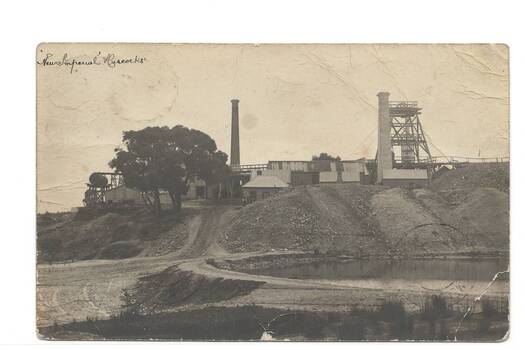 Mining buildings on hill above mullock heap, dam in foreground