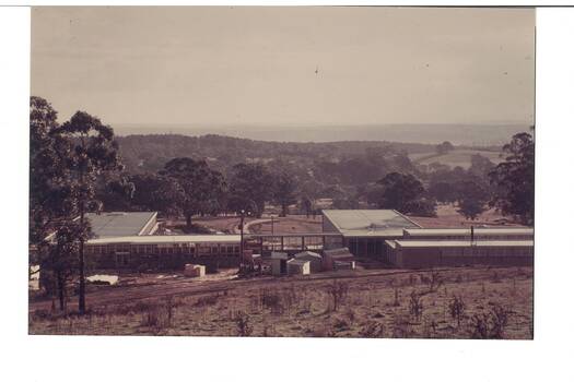 Looking down slope on construction site, low educational buildings, open ground
