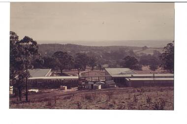 Looking down slope on construction site, low educational buildings, open ground