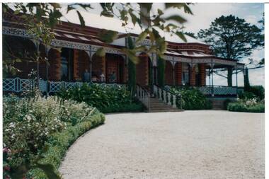 Single story brick Victorian house, veranda with lace and iron balustrades, gravel driveway, curved garden beds.