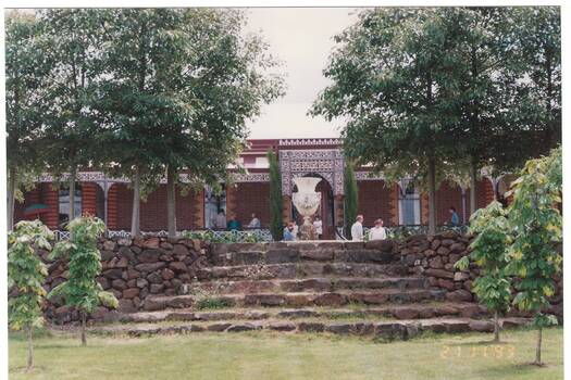 View up curved stone steps over patio to polychrome brick house, 