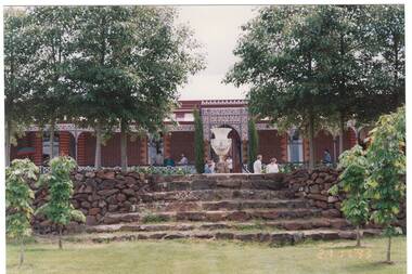 View up curved stone steps over patio to polychrome brick house, 