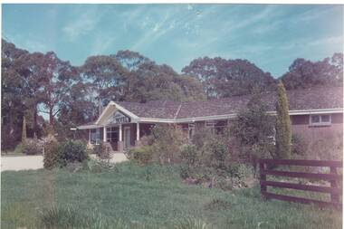 1970'2 style brick hotel, tile roof, driveway, native garden bed, large trees behind.